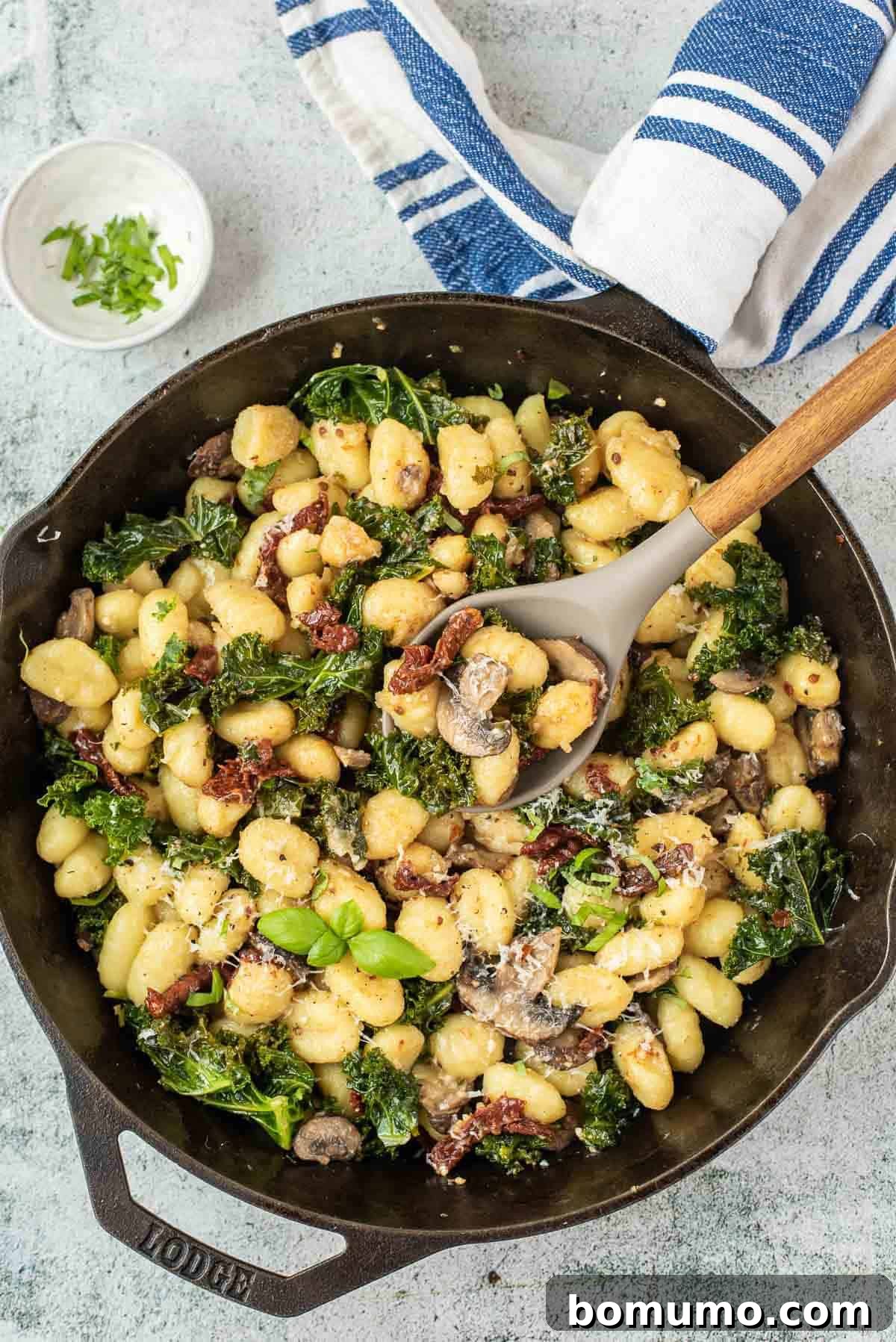 Overhead view of a black skillet filled with gnocchi with kale, sun-dried tomatoes, and mushrooms. A delicious vegetarian meal for weeknights.