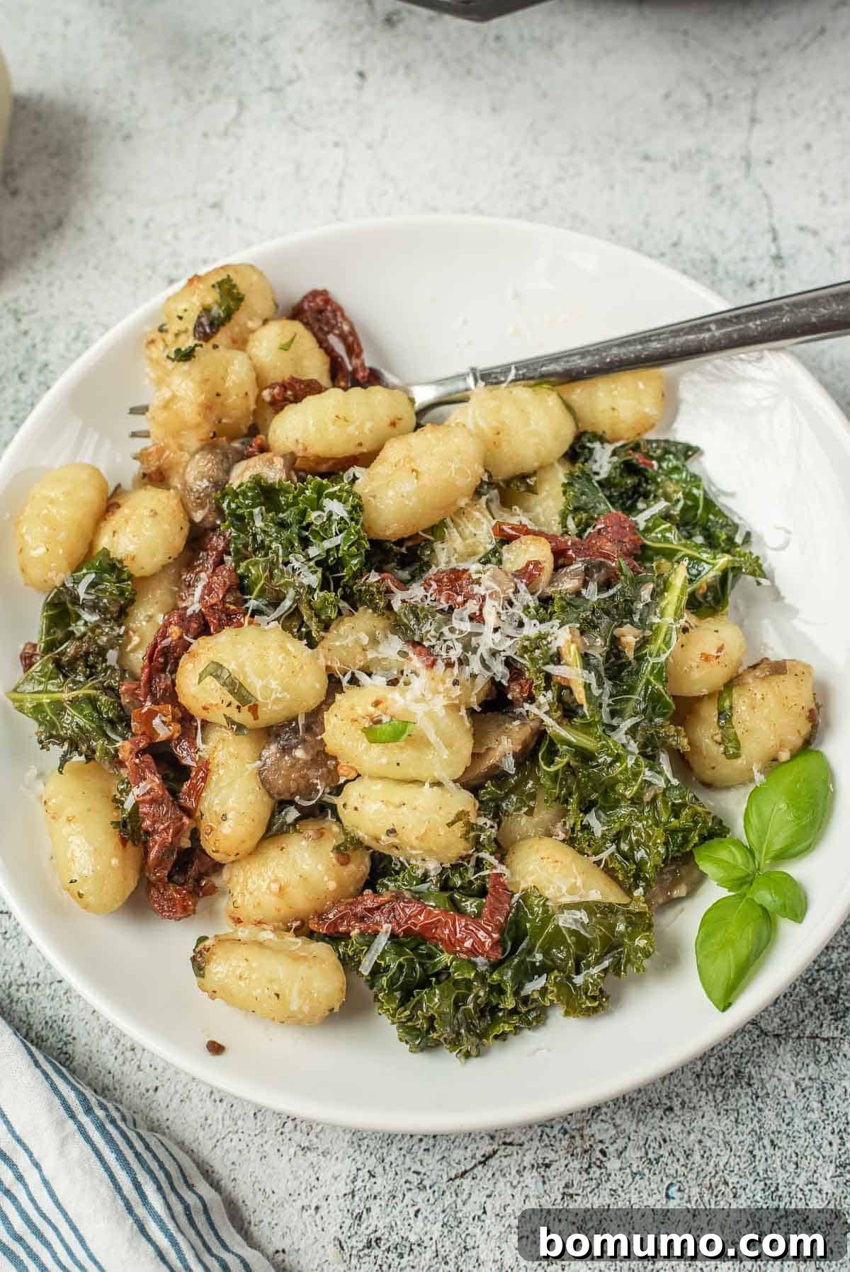Gnocchi on a white plate with kale, mushrooms, sun-dried tomatoes, and cheese, ready to be enjoyed.
