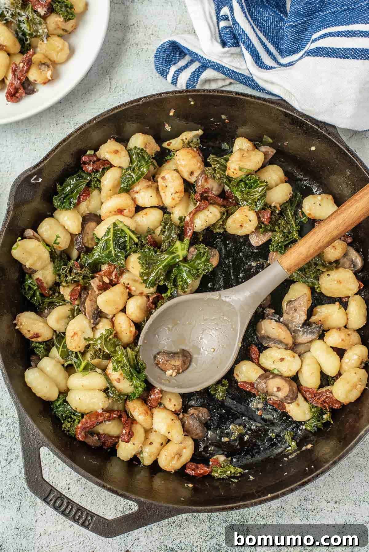 Black skillet half full of gnocchi, depicting it being served out of the skillet, ready for plates.