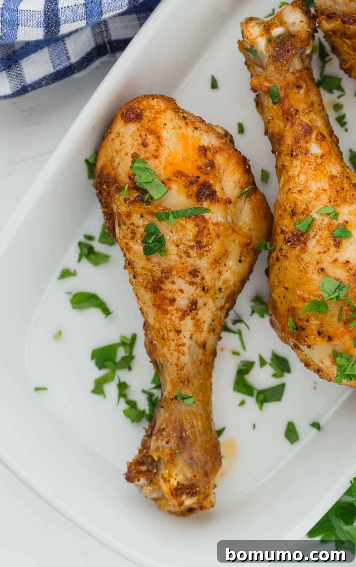 Overhead view of a golden-brown air fryer chicken drumstick on a white plate, garnished with fresh parsley.