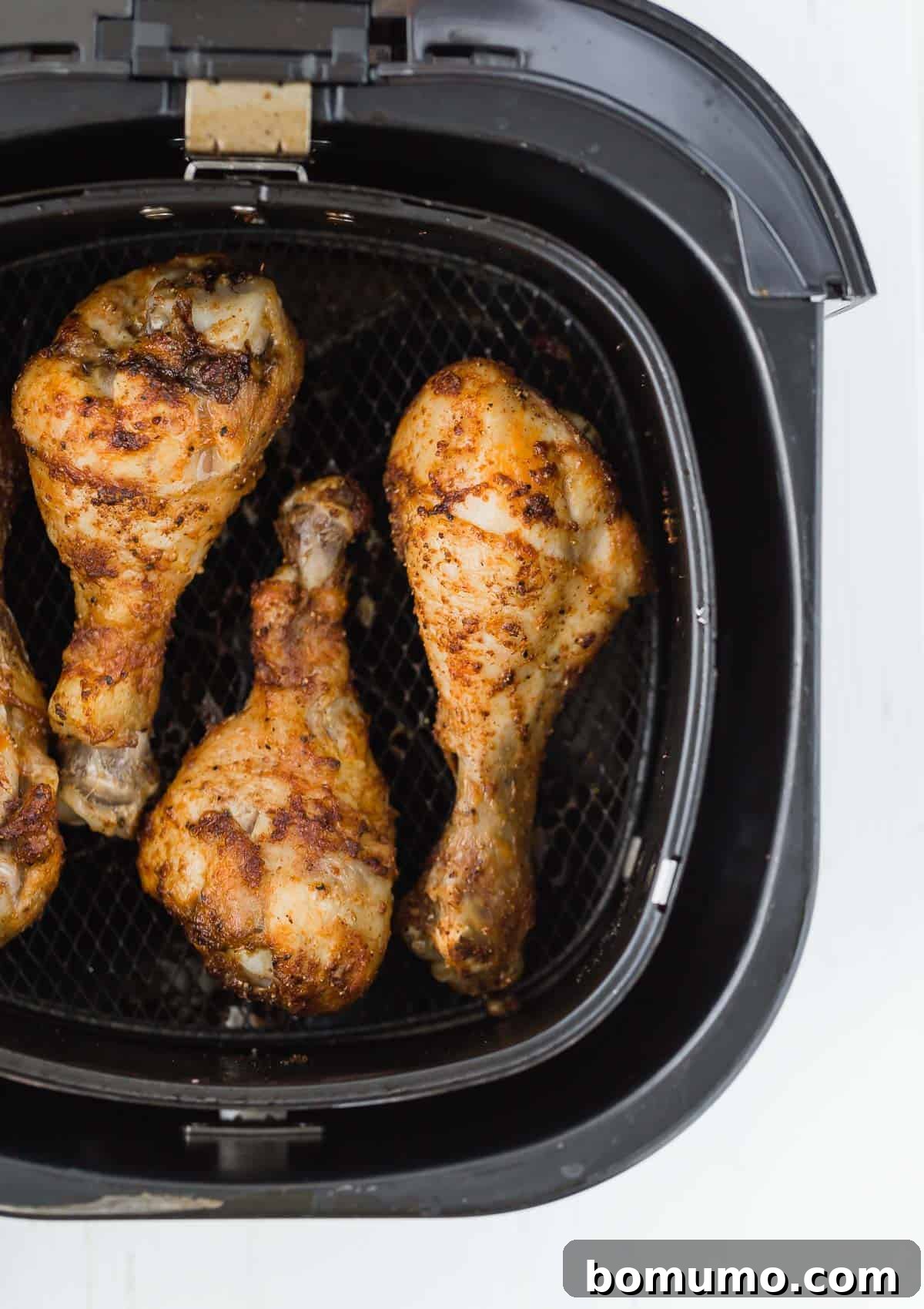 Overhead view of a black air fryer basket filled with beautifully cooked, golden-brown chicken drumsticks.