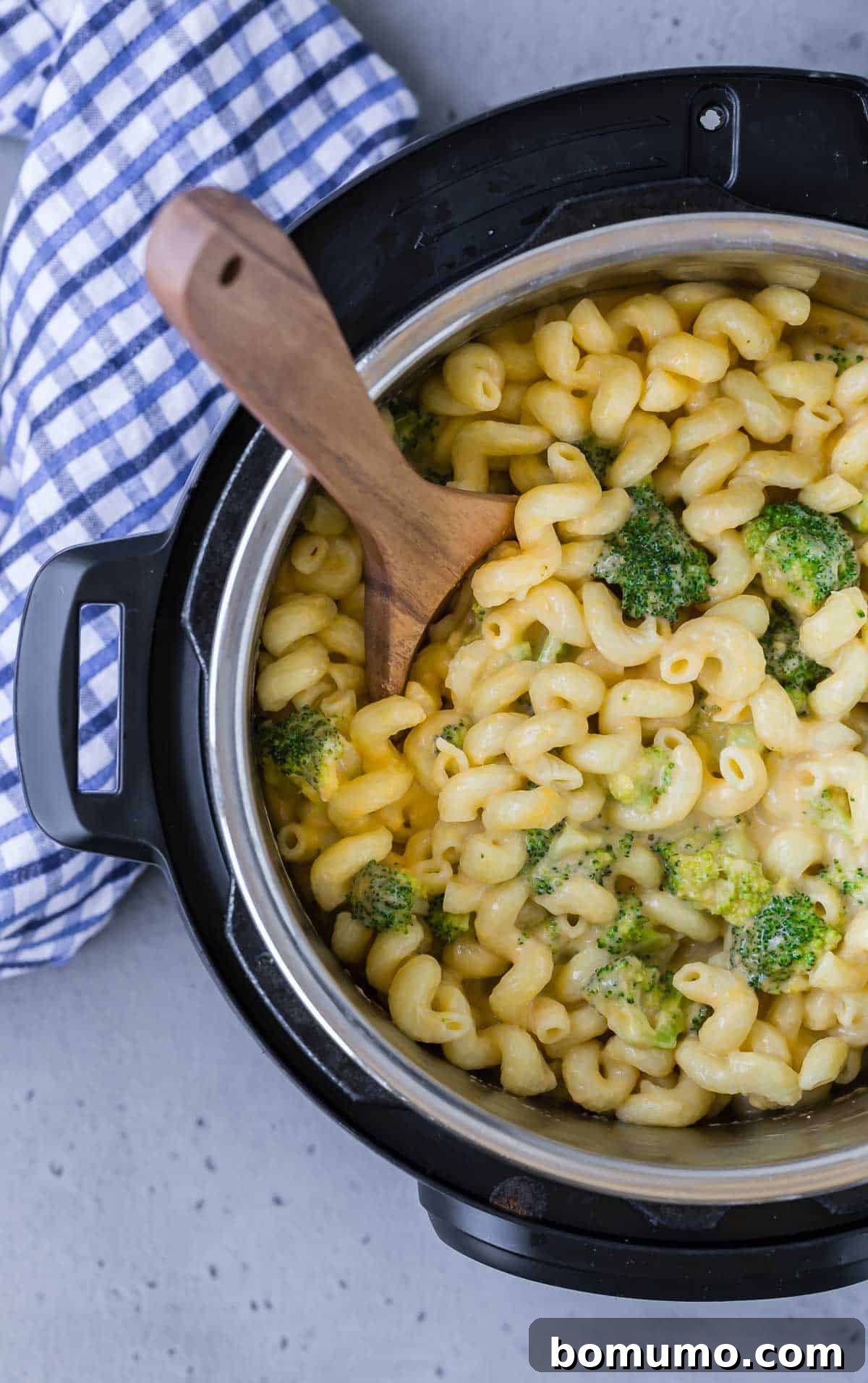 Overhead view of an instant pot pressure cooker filled with macaroni and cheese with broccoli. Wooden spoon also visible.