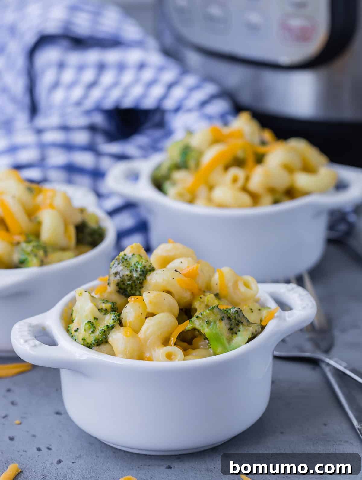 Three small white bowls filled with broccoli mac and cheese, with an instant pot in the background.