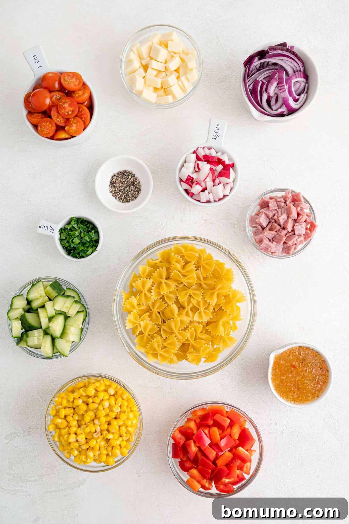 A vibrant selection of fresh ingredients laid out for summer pasta salad, including pasta, colorful bell peppers, tomatoes, cucumbers, and fresh herbs, ready for preparation.