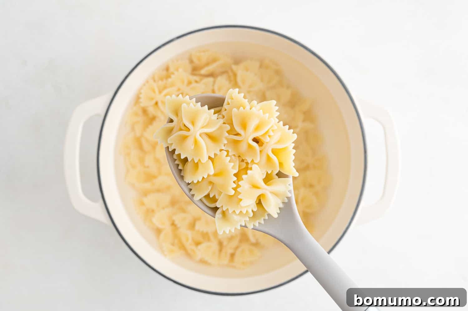 Freshly cooked pasta, drained and ready for the salad, displayed in a spoon and a pot.
