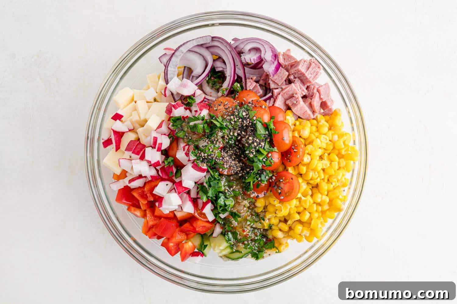 A vibrant summer pasta salad, with mini farfalle, colorful vegetables, and salami, before being tossed together.