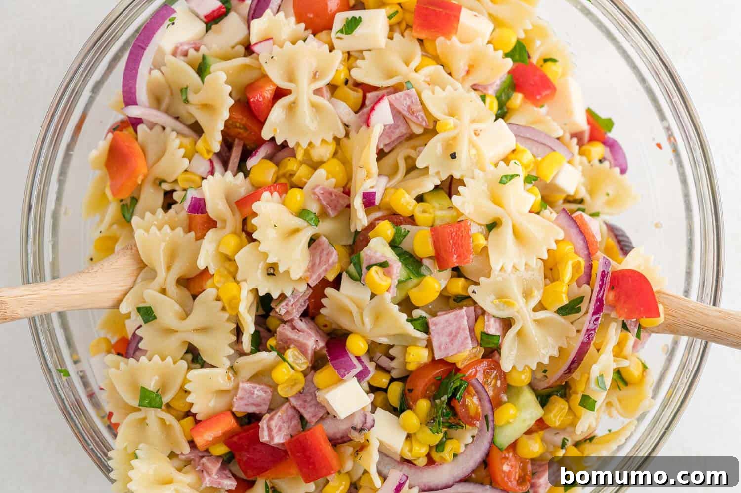 The summer pasta salad, made with charming mini farfalle, being expertly tossed to combine all ingredients and dressing.