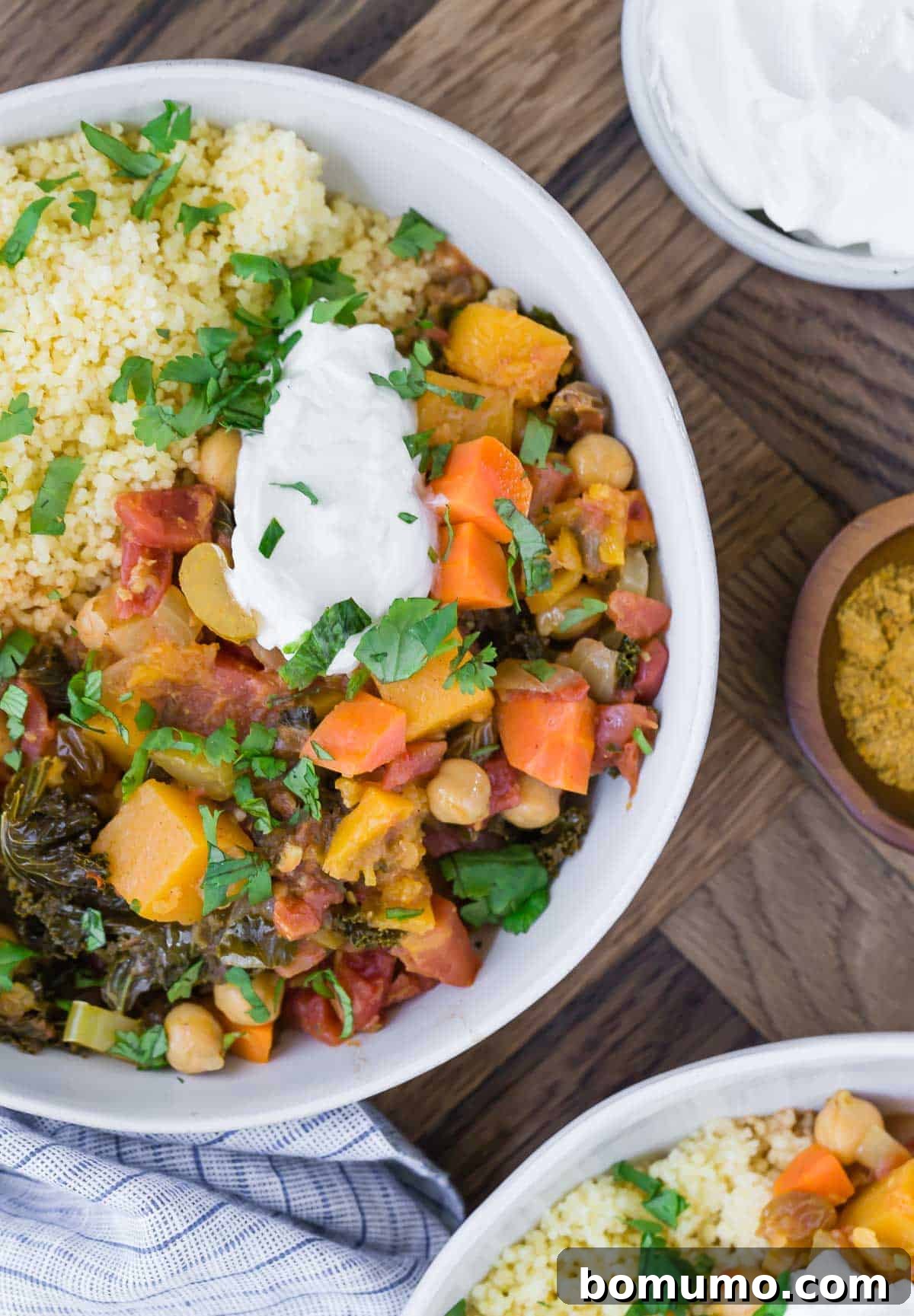Overhead view of moroccan stew with butternut squash and chickpeas in a white bowl. It is served with yogurt and couscous.