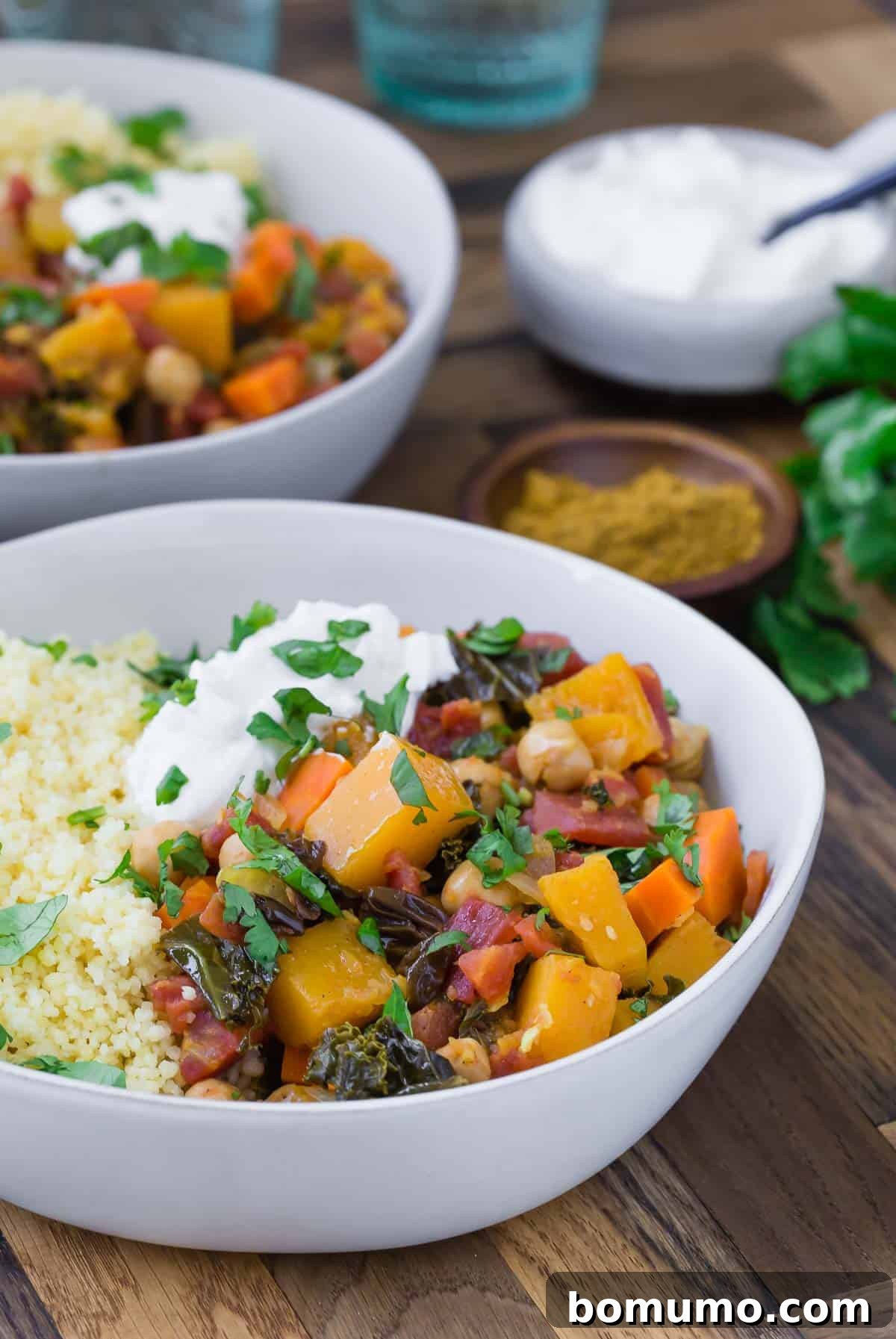 Two large white bowls with vegetarian moroccan squash stew with a small bowl of yogurt and fresh cilantro also pictured.