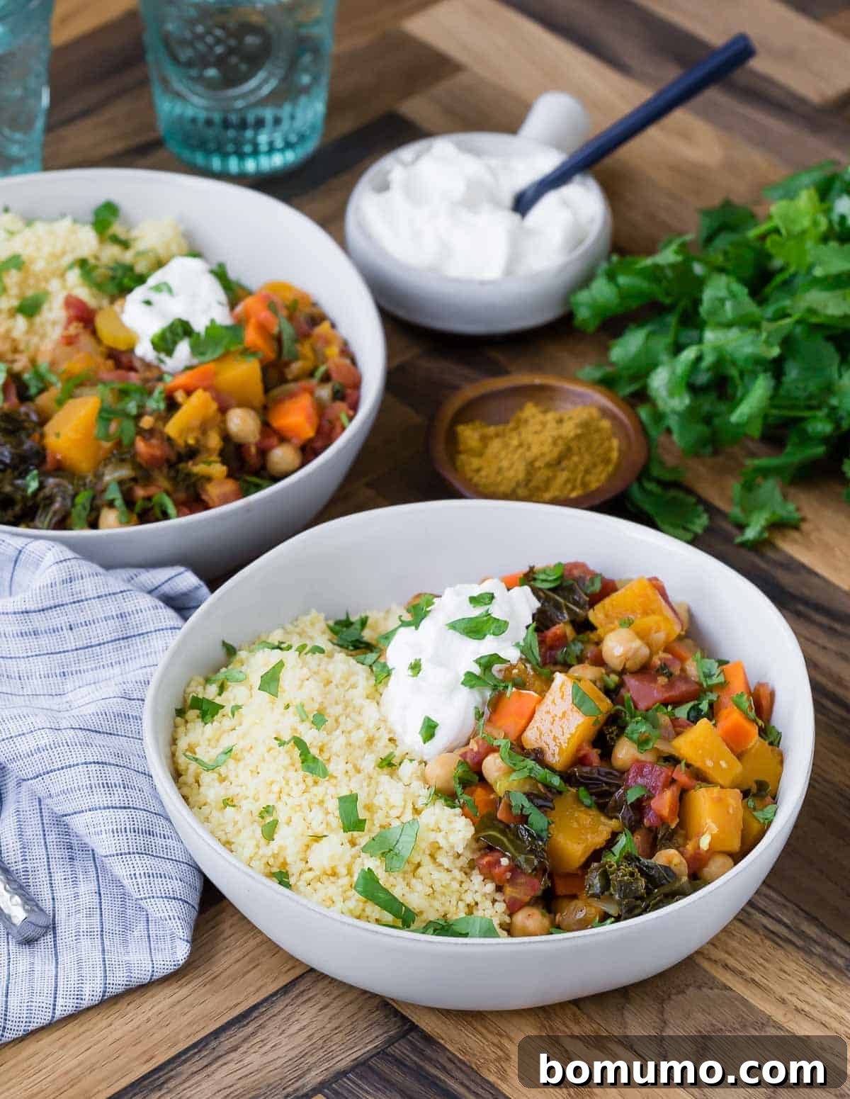 Two bowls of hearty vegetarian stew served over couscous and garnished with greek yogurt.