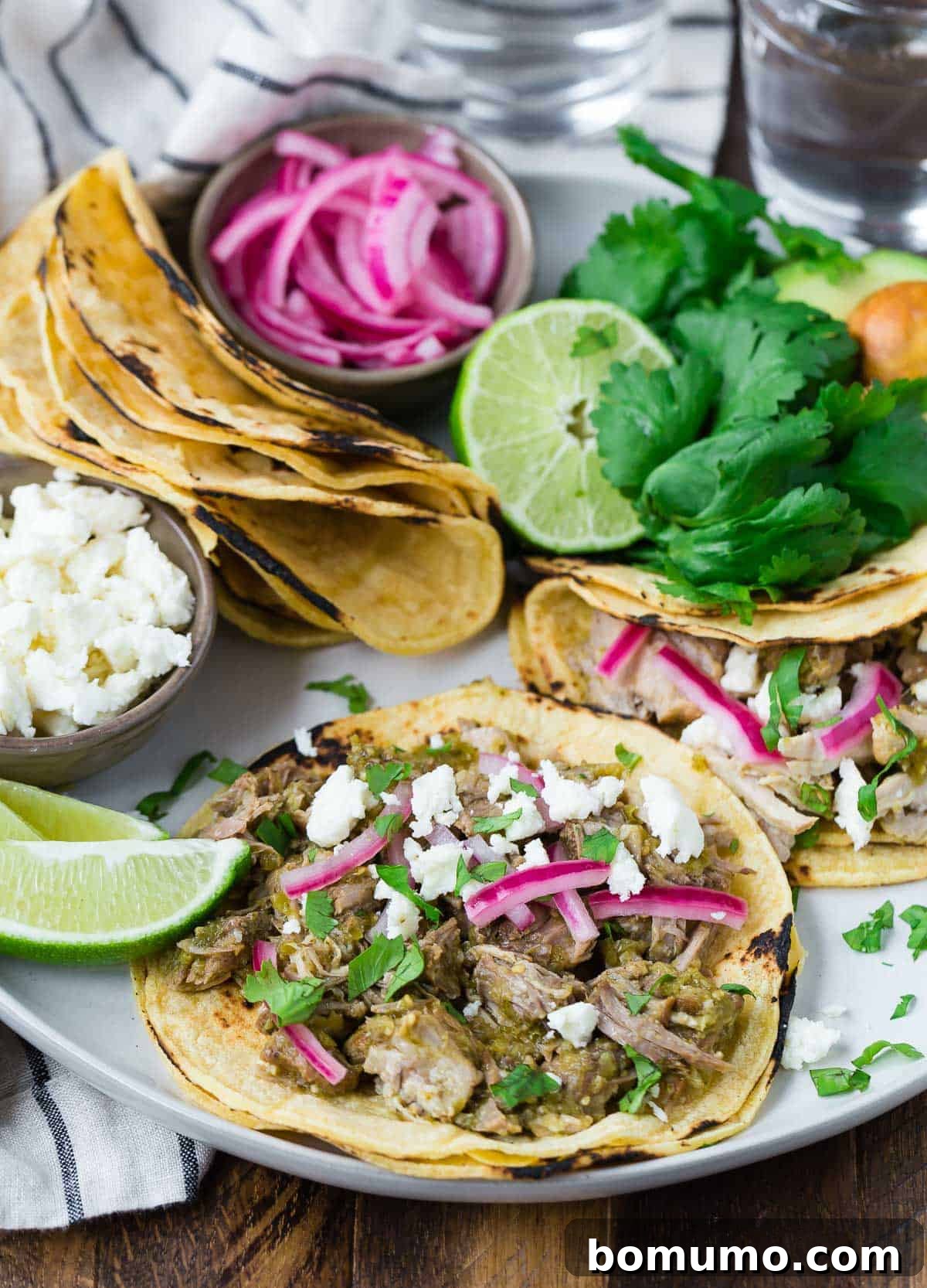 Amazing slow cooker pork tacos on a plate with assorted toppings.
