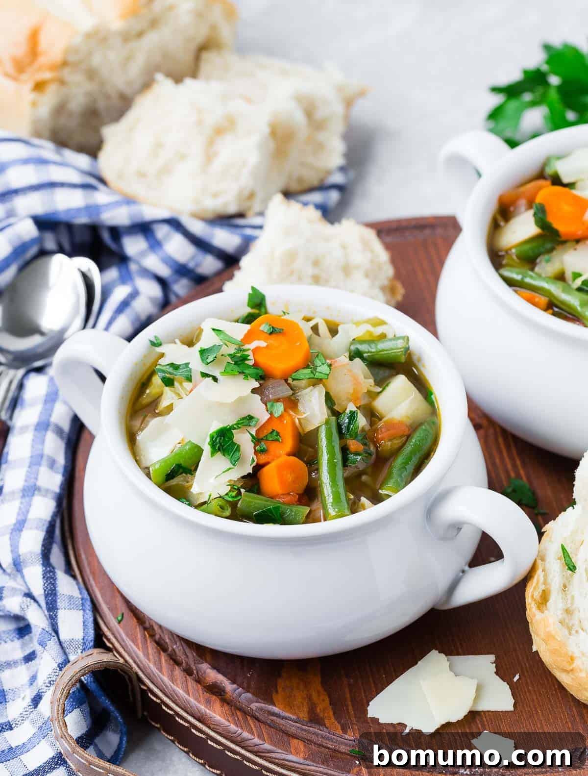 Two steaming bowls of homemade vegetable soup on a wooden tray, served with slices of rustic bread.