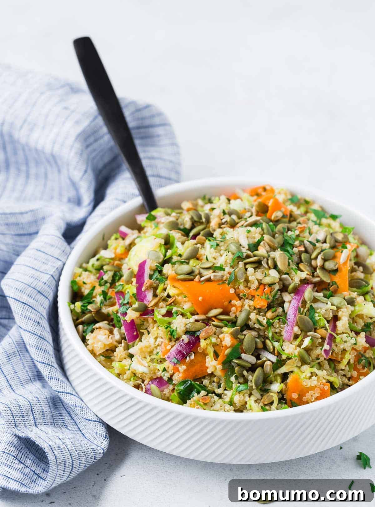 Hearty vegan quinoa salad served in a white bowl with a black spoon, set against a light grey background.