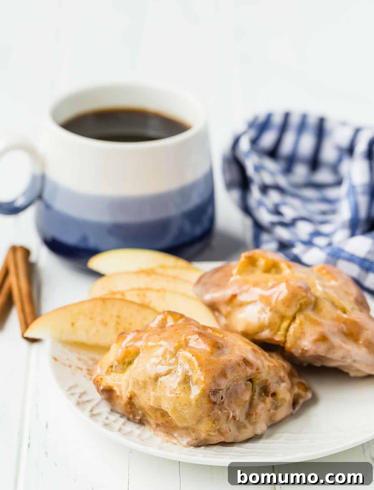 Apple fritters on a white plate with coffee in the background.