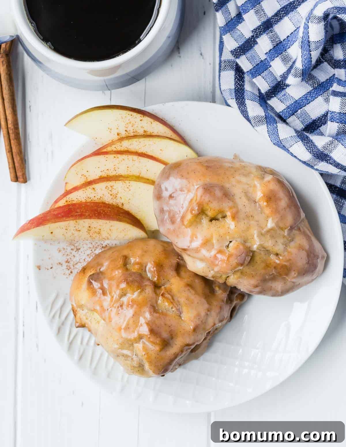 Overhead view of glazed apple fritters on a plate, with apples.