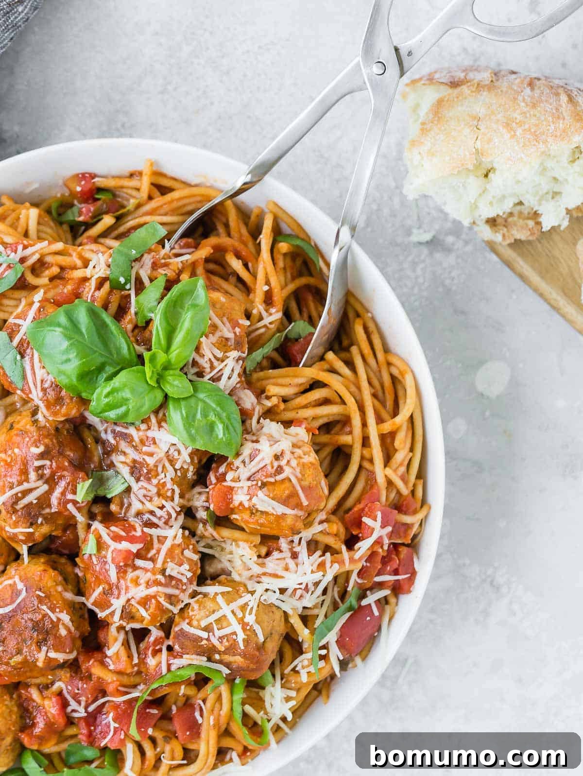 Large white bowl of spaghetti and meatballs, garnished with cheese and fresh basil.