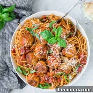 Overhead view of large white bowl full of spaghetti and meatballs, garnished with fresh basil.