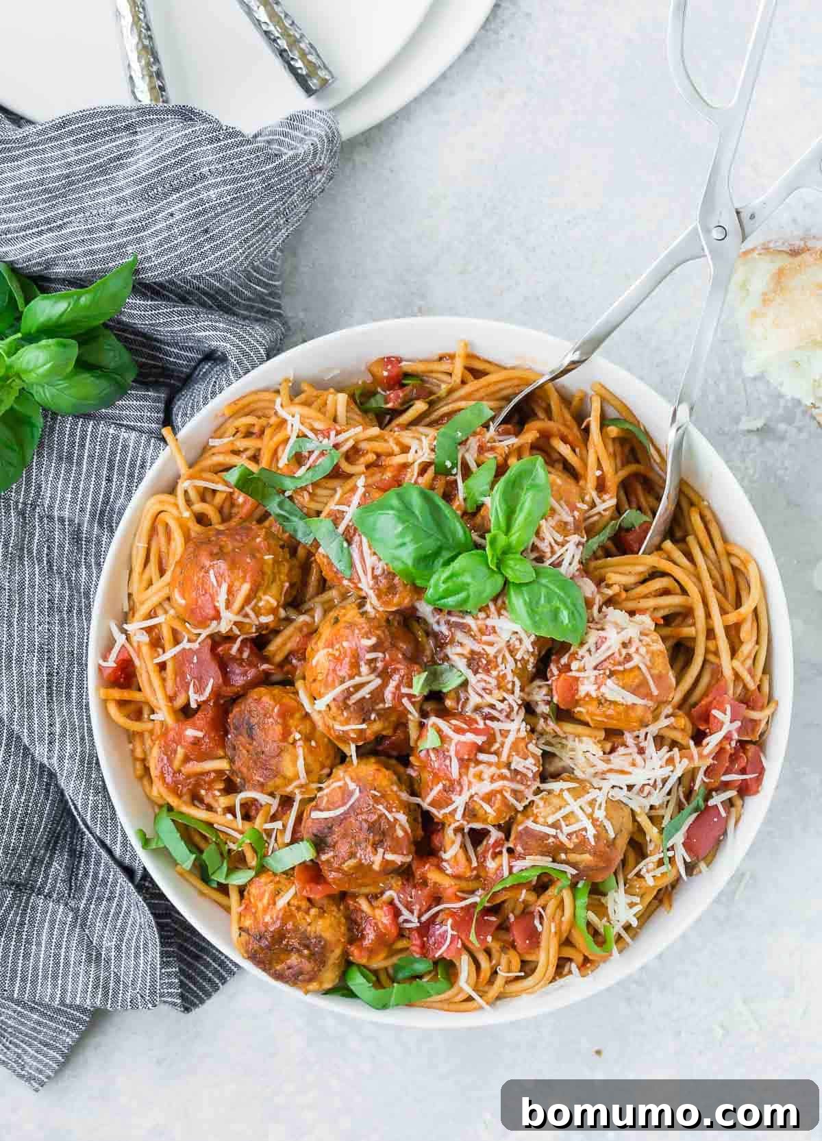 Overhead view of a white bowl with spaghetti, meatballs, and a tomato sauce.
