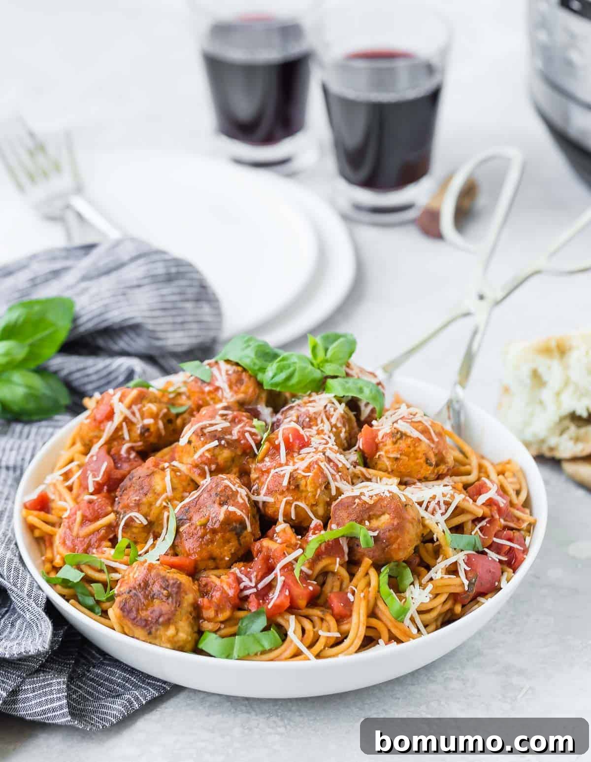 Spaghetti and meatballs with two glasses of wine in the background.