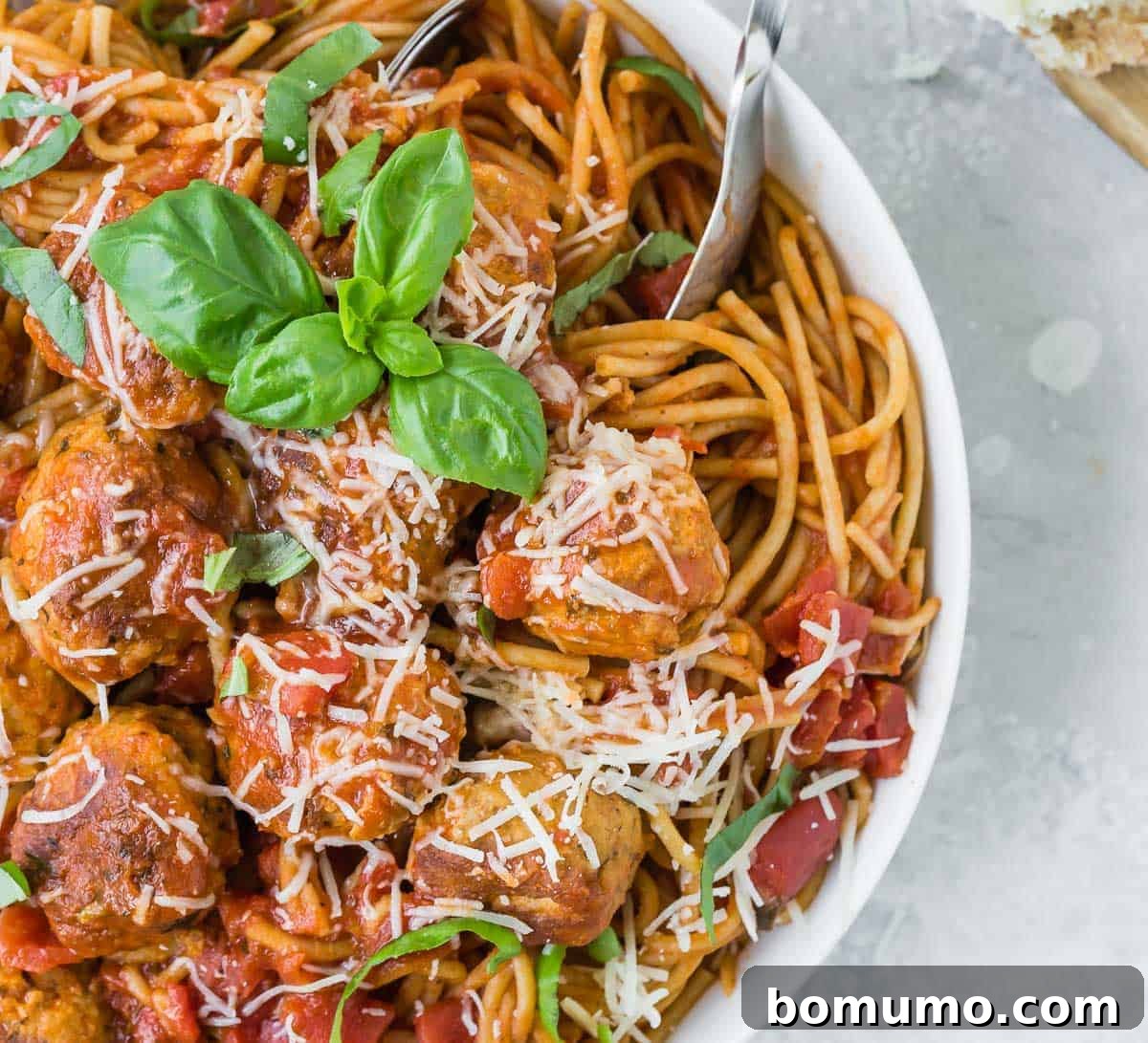 Close up overhead view of spaghetti and meatballs in a white bowl with fresh basil.