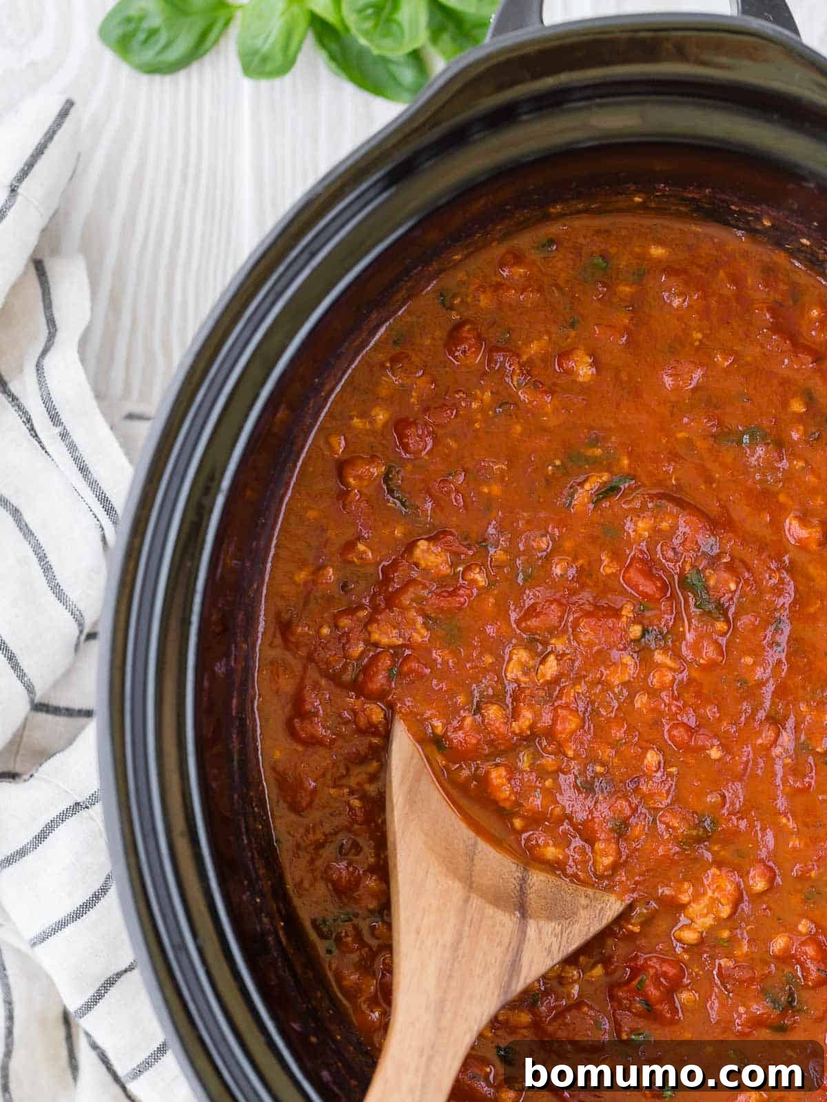 A close-up view of the rich, simmering spaghetti sauce in a slow cooker, with a wooden spoon partially submerged, showcasing its inviting texture.