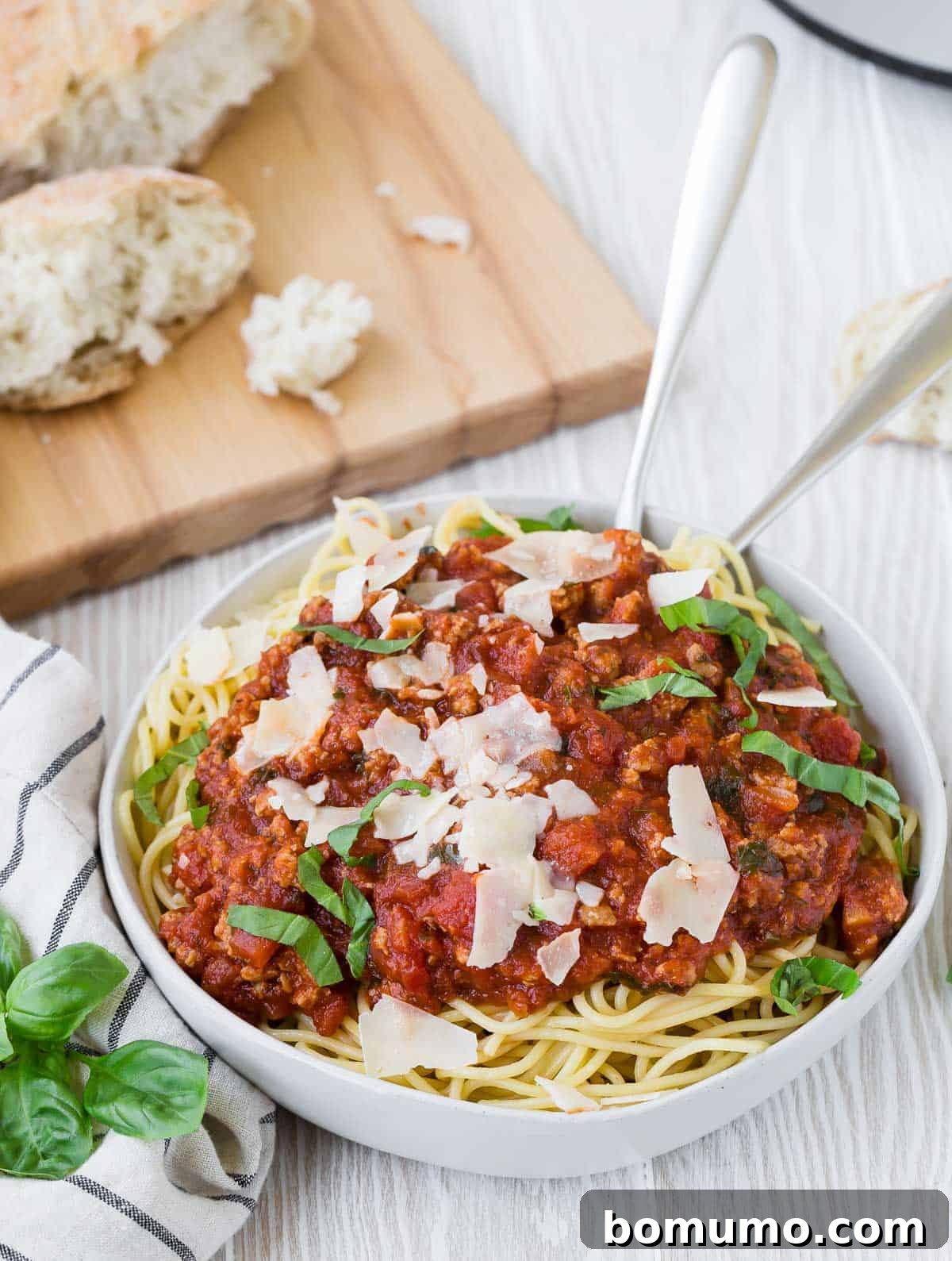 A gourmet presentation of spaghetti and meat sauce in a pristine white bowl, elegantly garnished with fresh basil leaves and freshly grated Parmesan cheese.