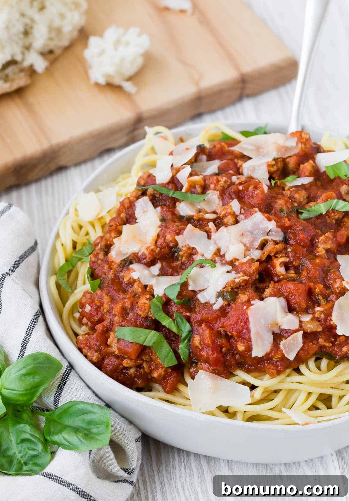 A generous serving of spaghetti covered in rich sauce and sprinkled with Parmesan cheese, presented in a clean white bowl.