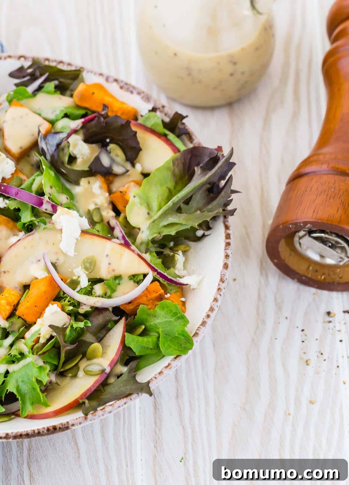Colorful fall salad with creamy dressing, a tipped over pepper mill also pictured, hinting at fresh ingredients.