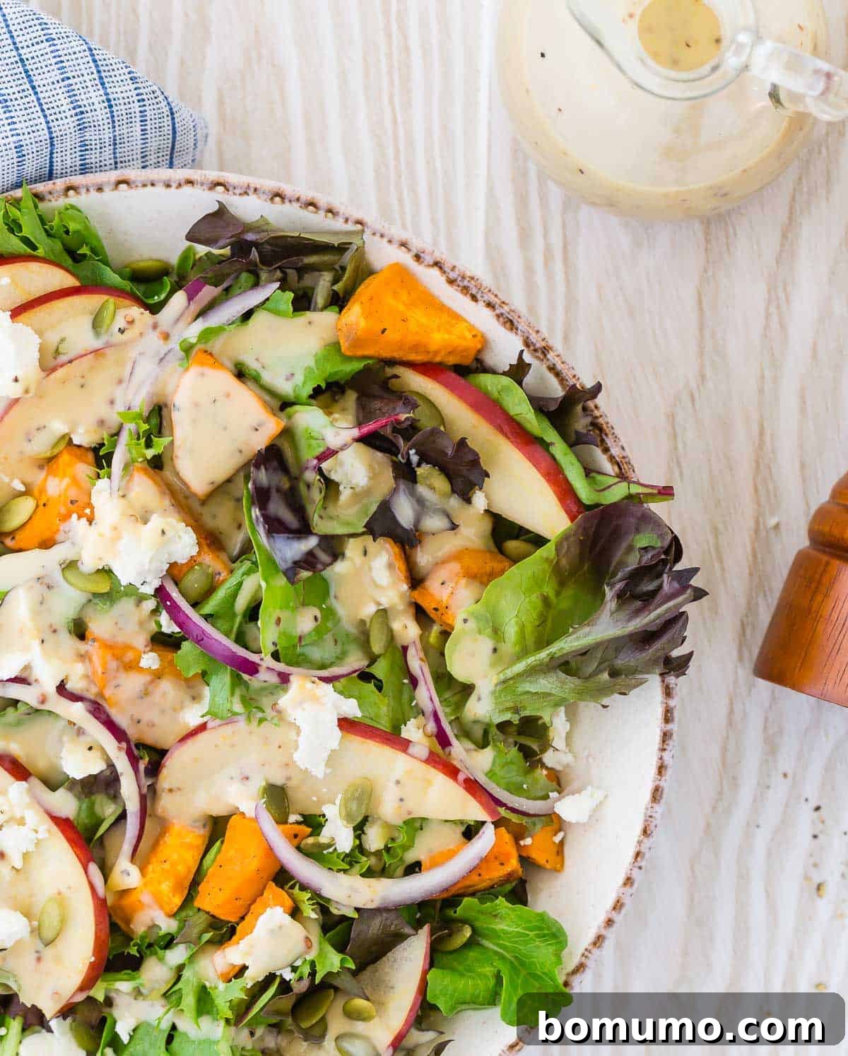 Colorful fall harvest salad with a creamy dressing on a light wood background, featuring vibrant ingredients.