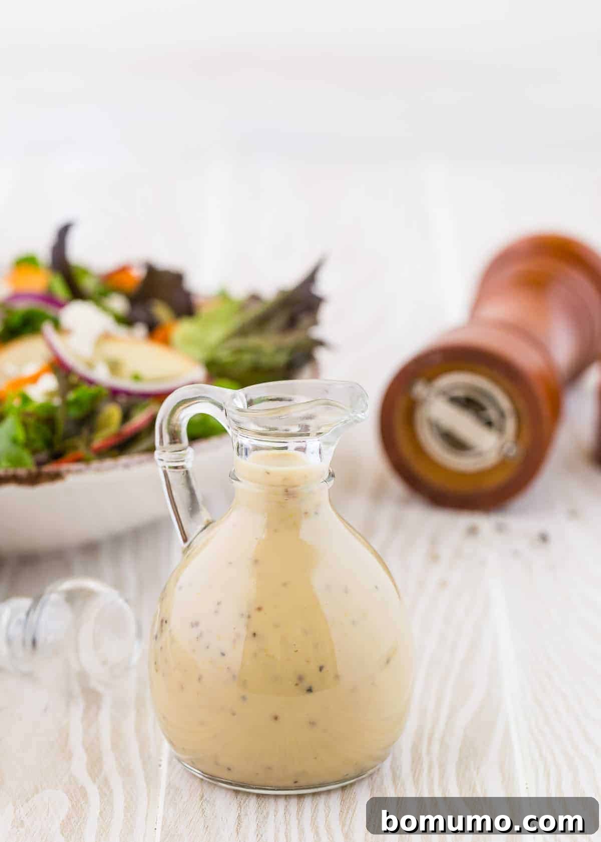 Creamy maple black pepper dressing in a small glass jar with a pour spout and handle, ready to serve.