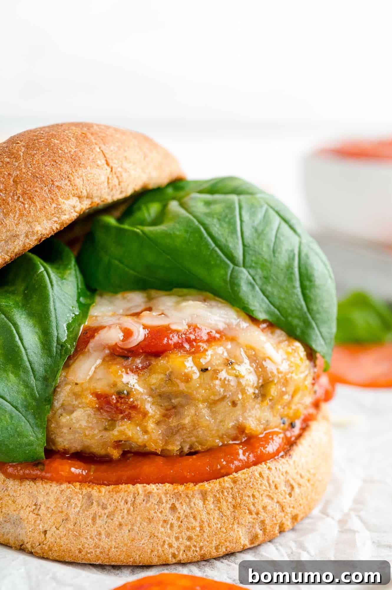 A close-up view of a pizza turkey burger, with the top bun subtly slid to the side to reveal the mouthwatering layers of melted cheese, rich sauce, and fresh basil within.