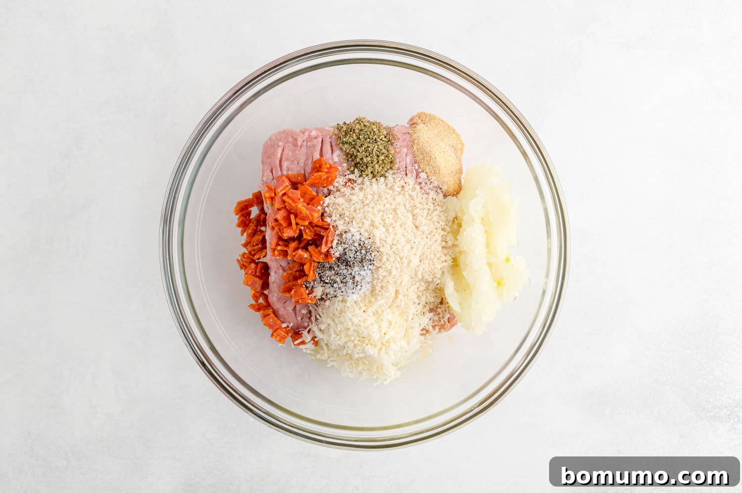 A clear glass bowl filled with the unmixed ingredients for pizza turkey burgers, showcasing their freshness and readiness for combination.