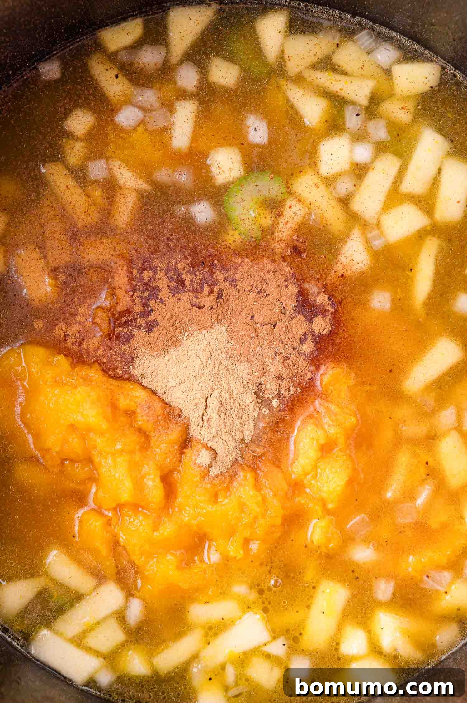 Chopped onions, apples, cooked squash, broth, and spices in a pot, ready to be mixed and cooked.