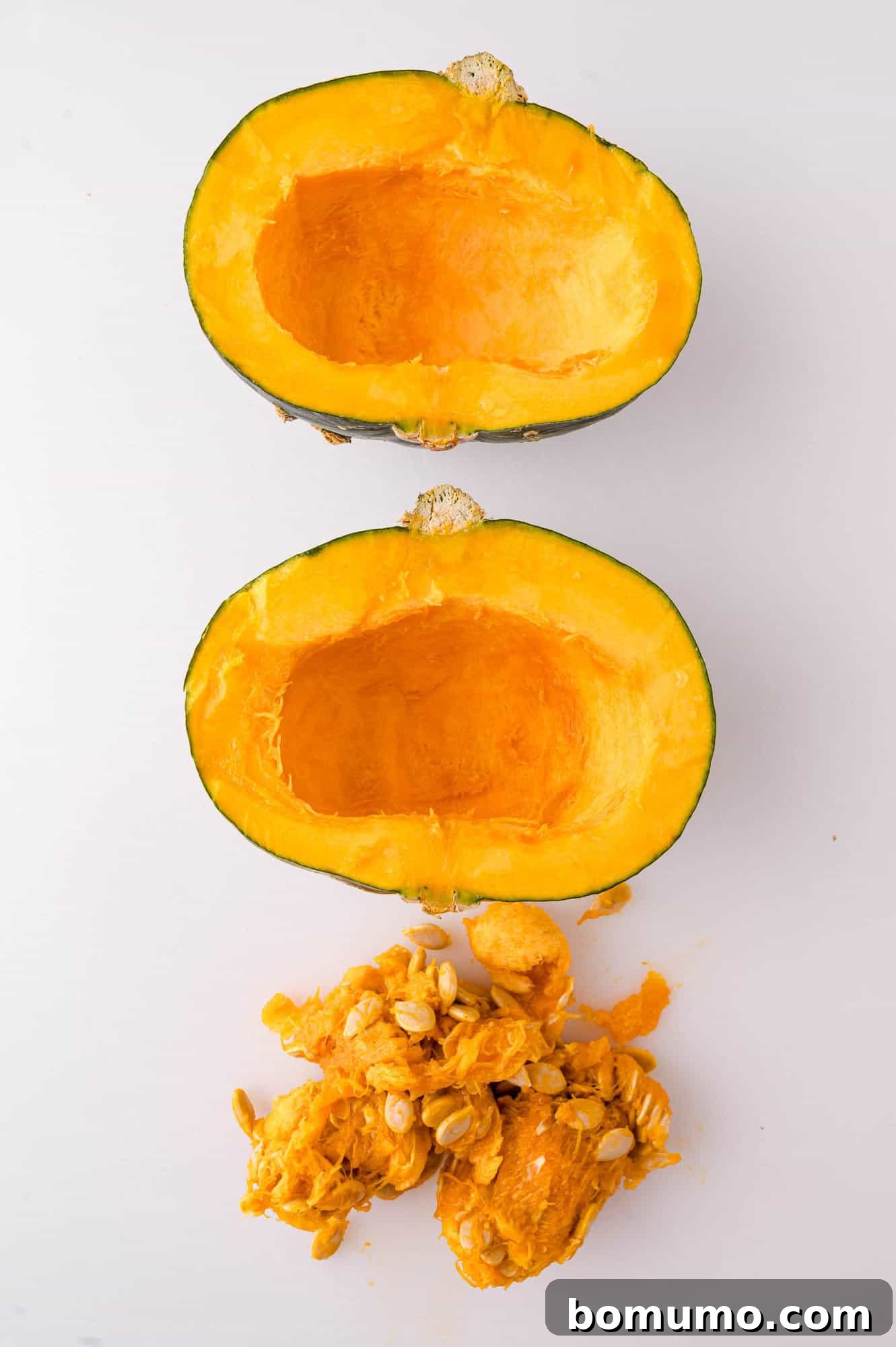 A kabocha squash cut in half with seeds and fibrous pulp removed, displayed on a white surface.