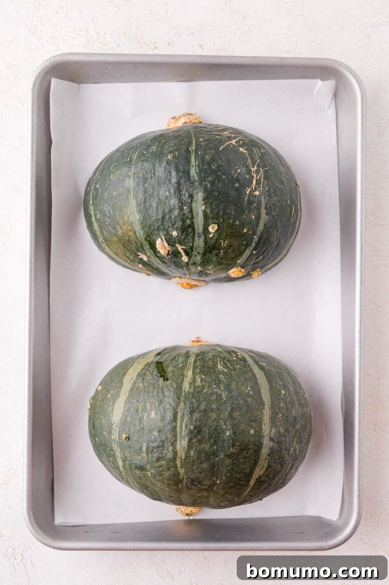 Two whole green squash halves placed side by side on a parchment-lined baking tray.