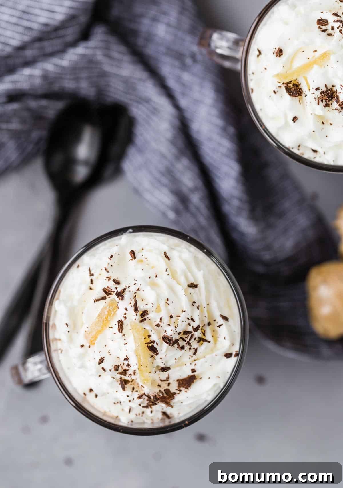 An overhead view of two mugs of hot chocolate, generously topped with whipped cream, ready to be enjoyed.