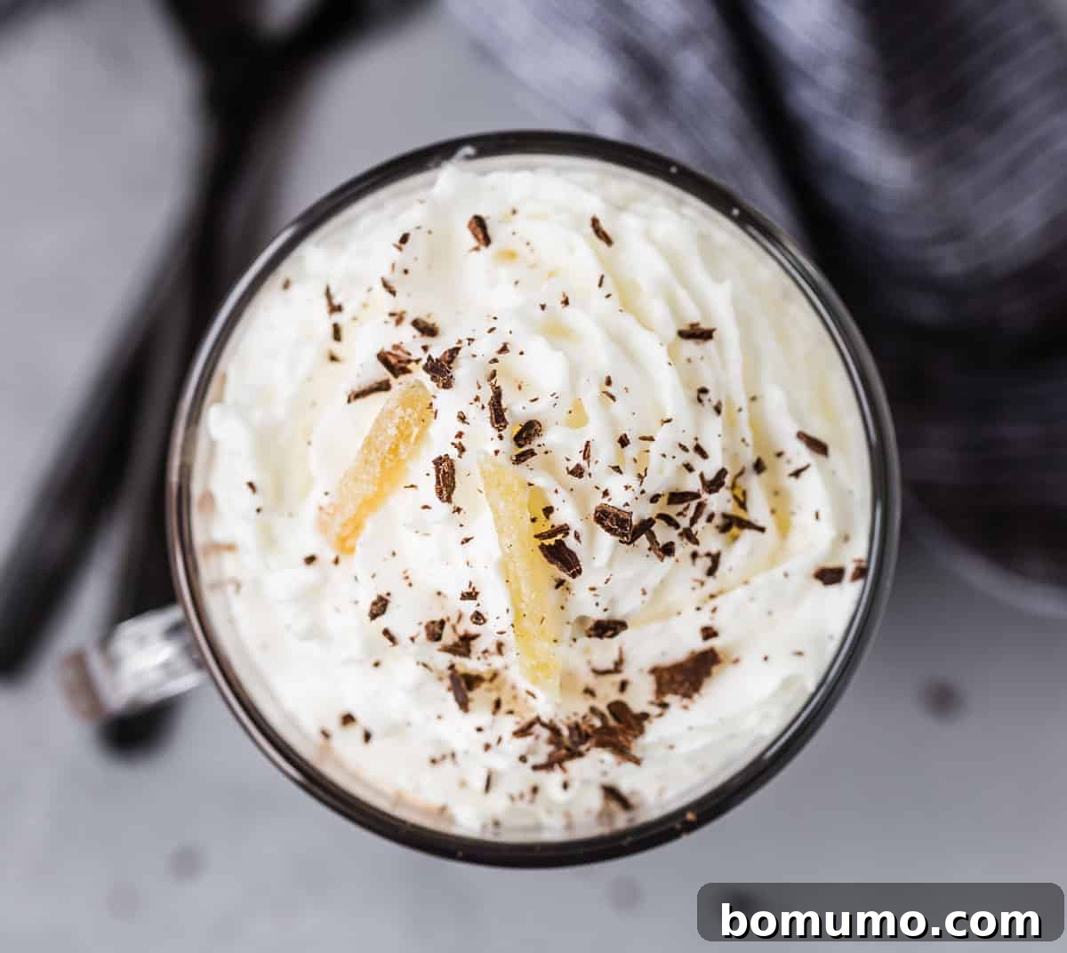 An inviting overhead view of whipped cream-topped cocoa, beautifully garnished with rich chocolate shavings and delightful candied ginger.