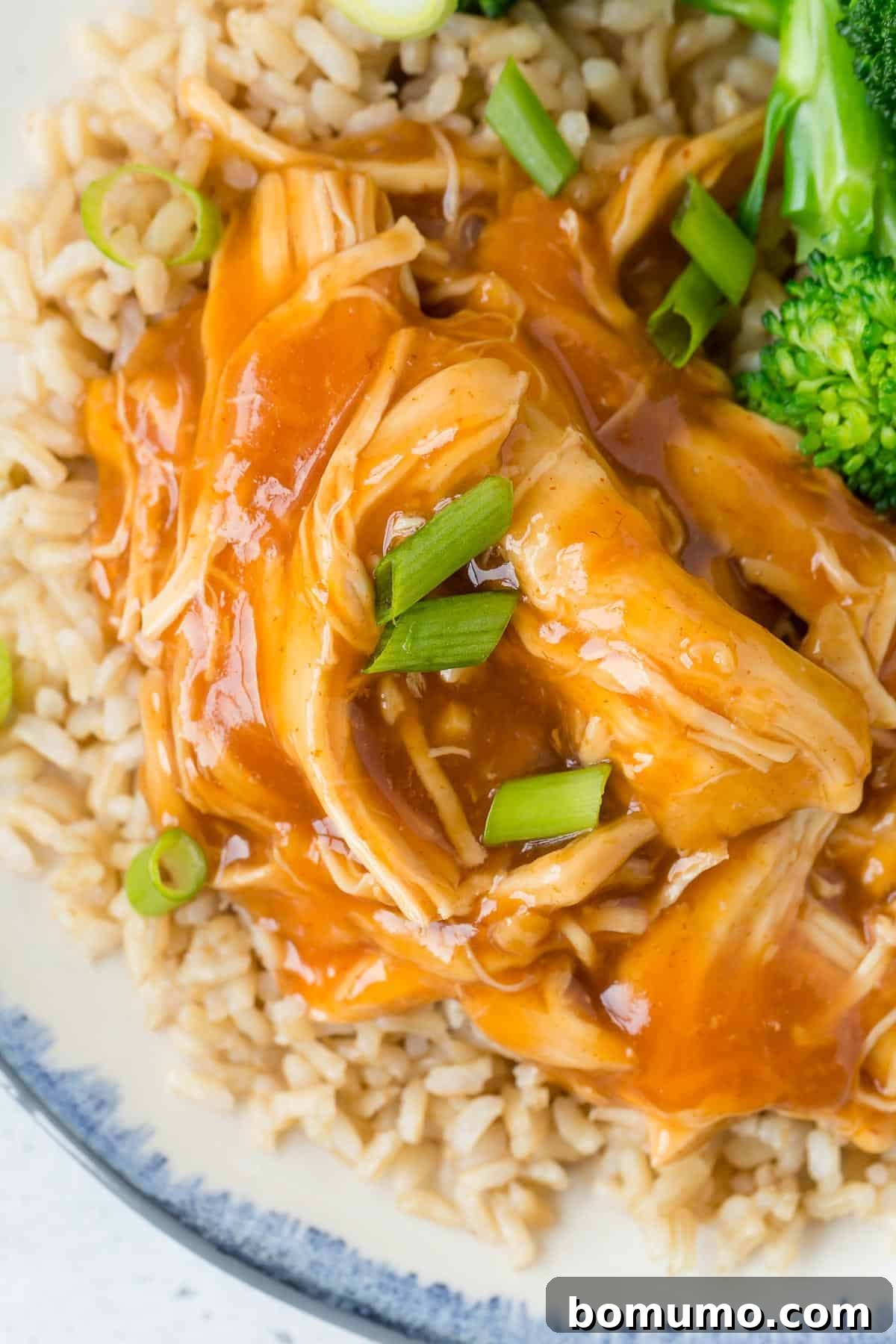 Close up view of pulled chicken with a honey sriracha sauce, served with rice and broccoli.