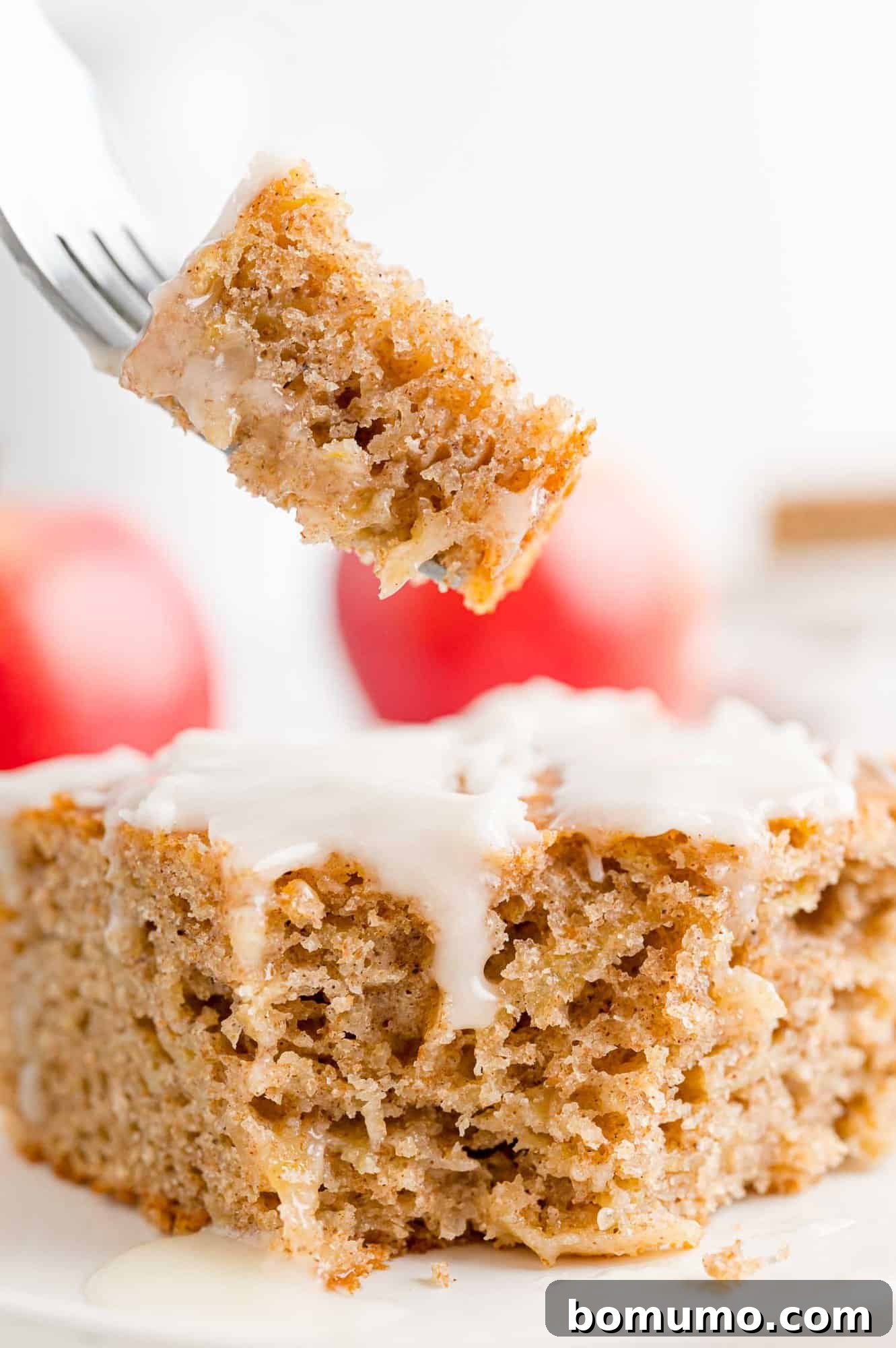 A fork lifting a bite from a slice of glazed apple spice cake on a plate.