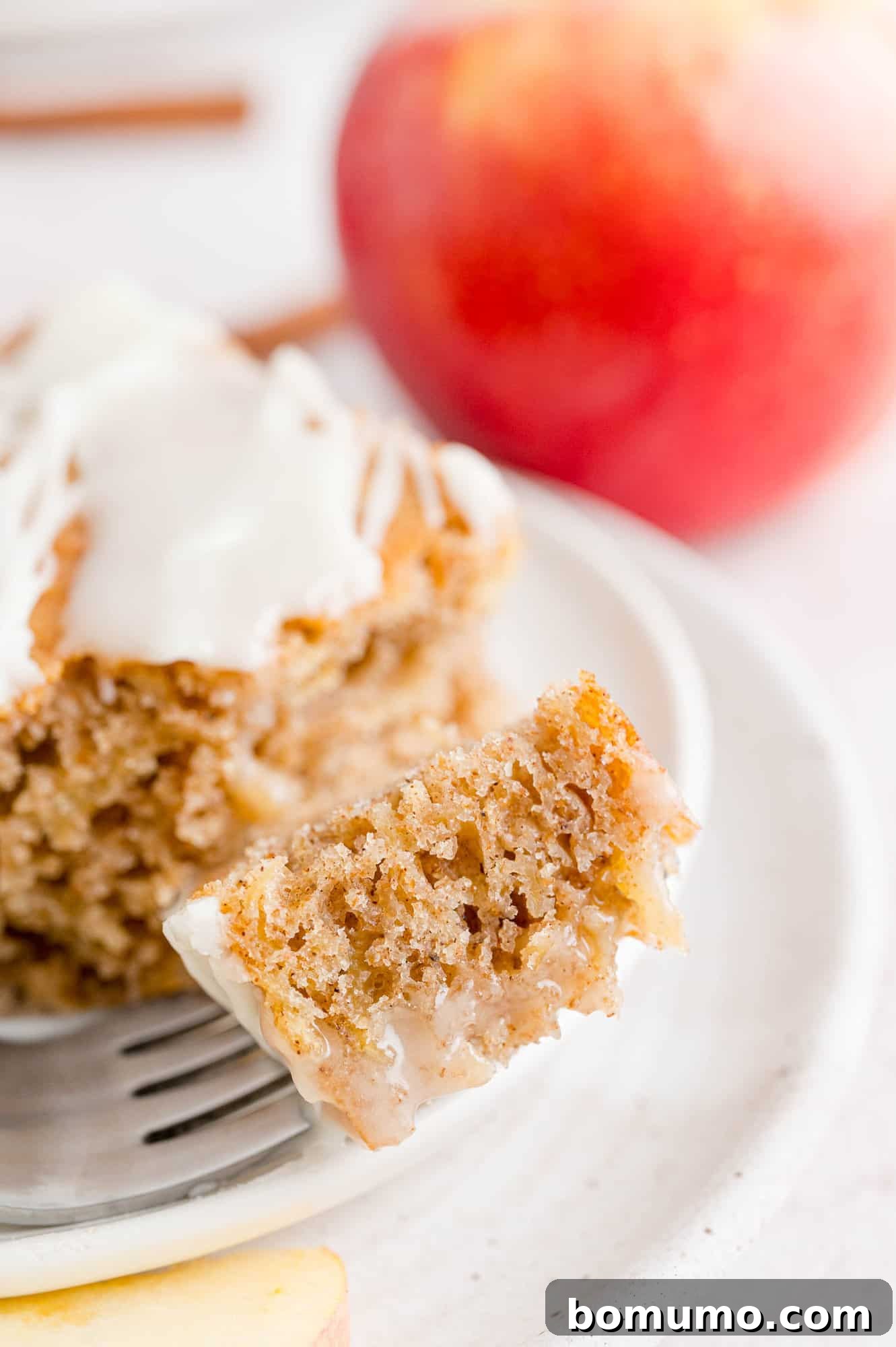 A forkful of cake resting next to a slice of apple spice cake on a plate.