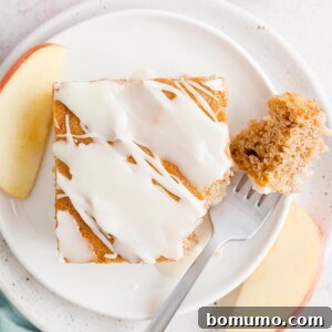 Overhead view of a slice of apple spice cake on a plate with a forkful missing.