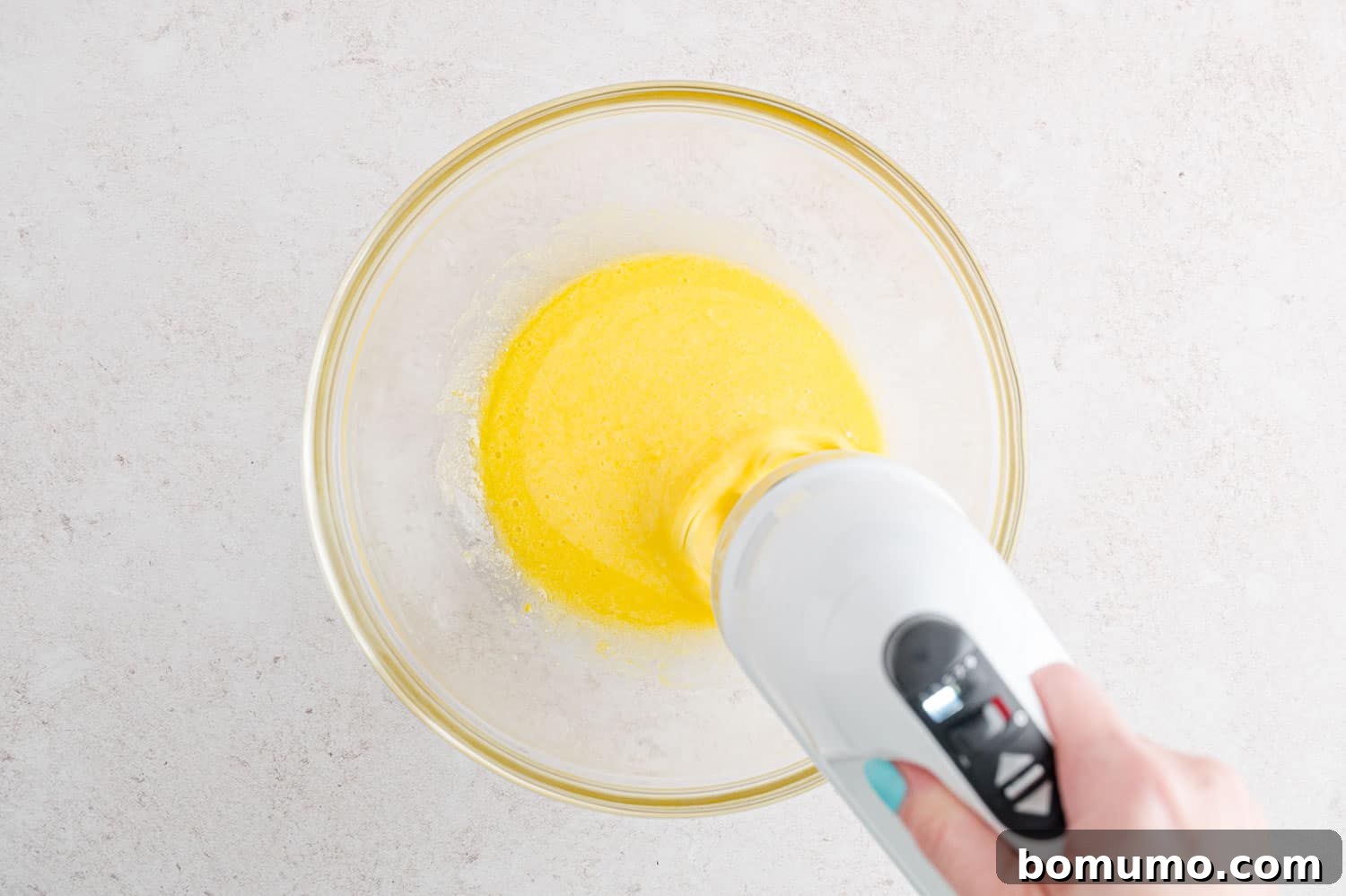 A hand using a hand mixer to beat wet ingredients in a bowl.