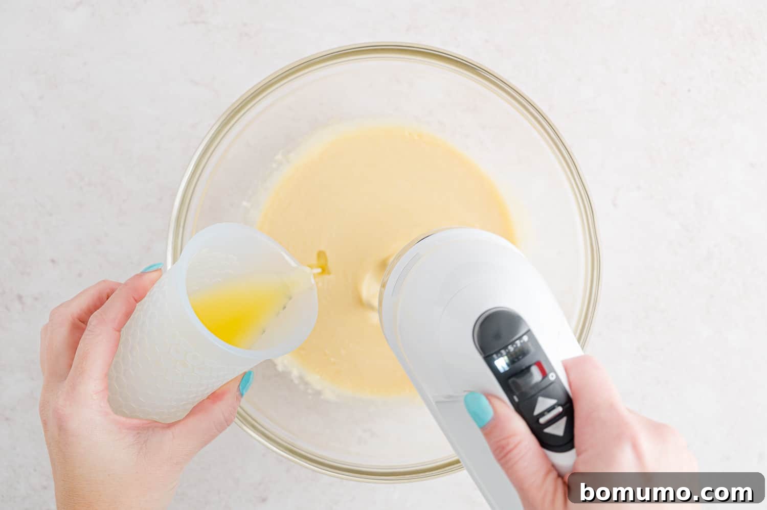 One hand streaming meted butter into a bowl of wet cake batter ingredients while the other hand blends with a hand mixer.
