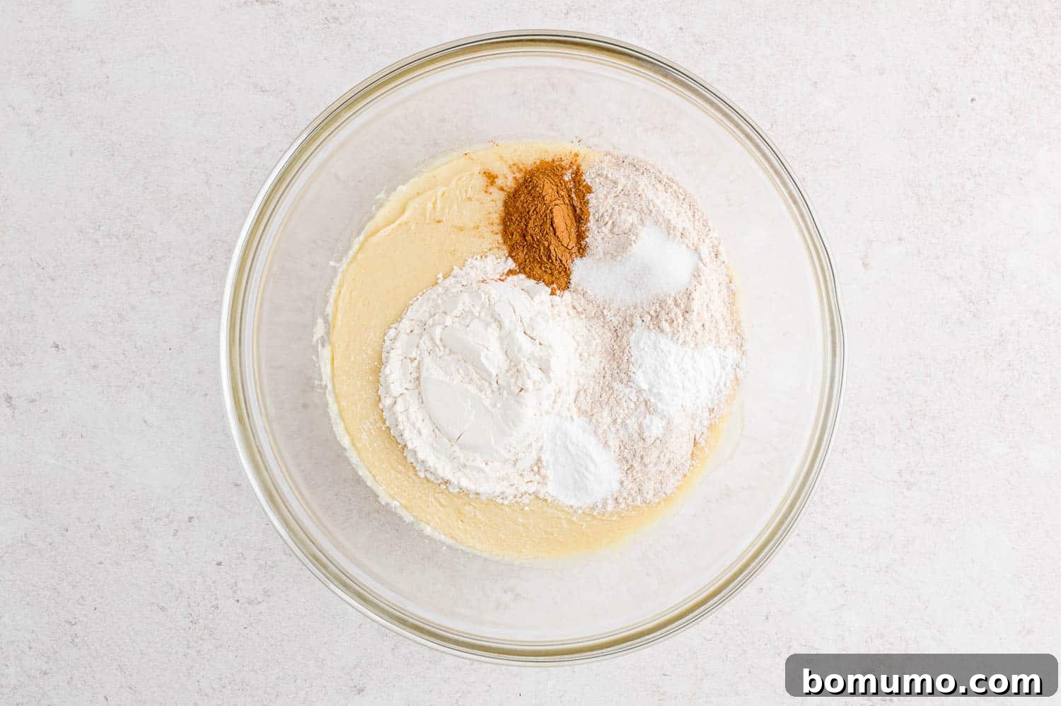 Dry cake batter ingredients added to a bowl with wet ingredients.