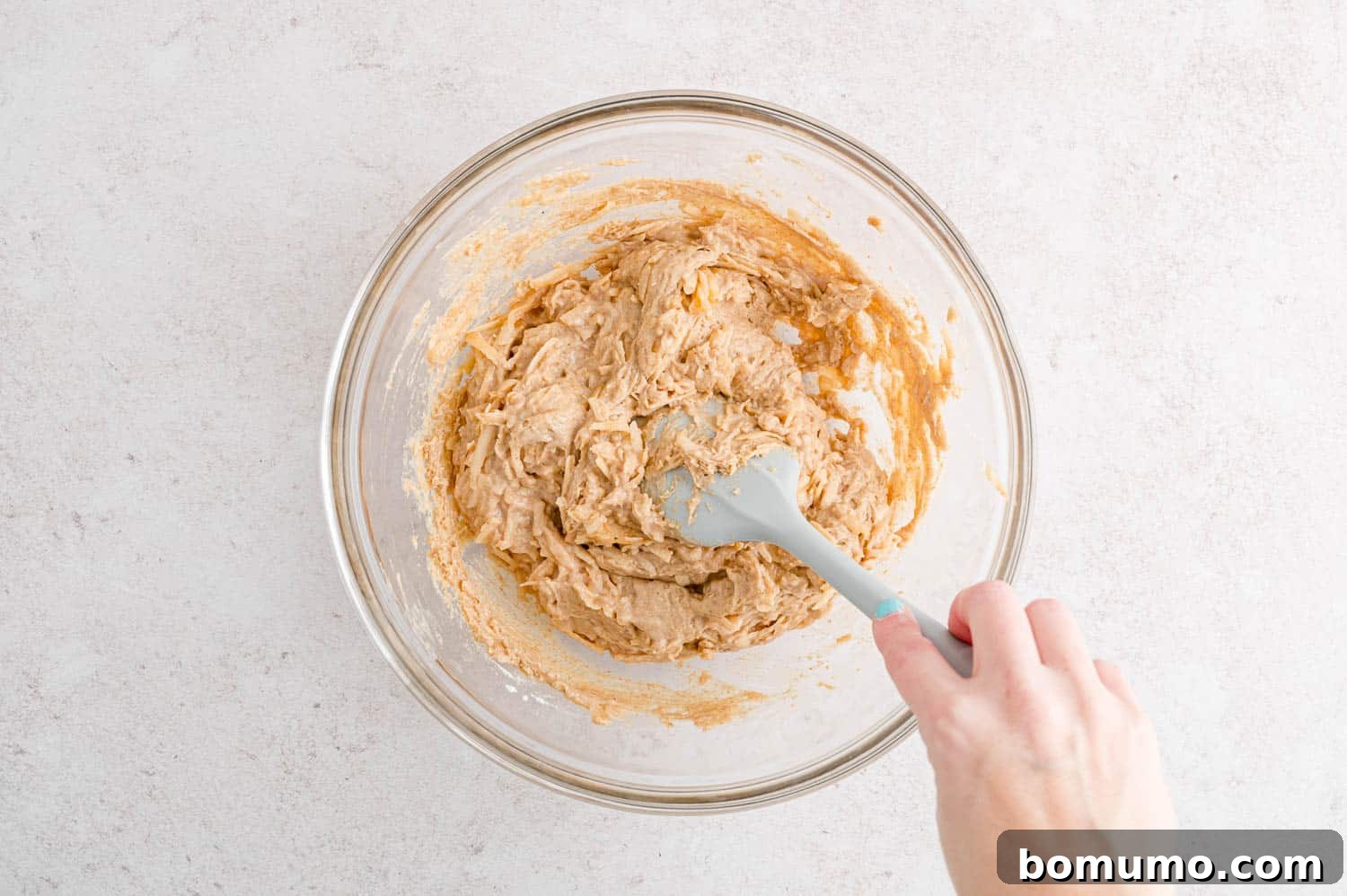 A hand stirring the batter for apple spice cake in a bowl.