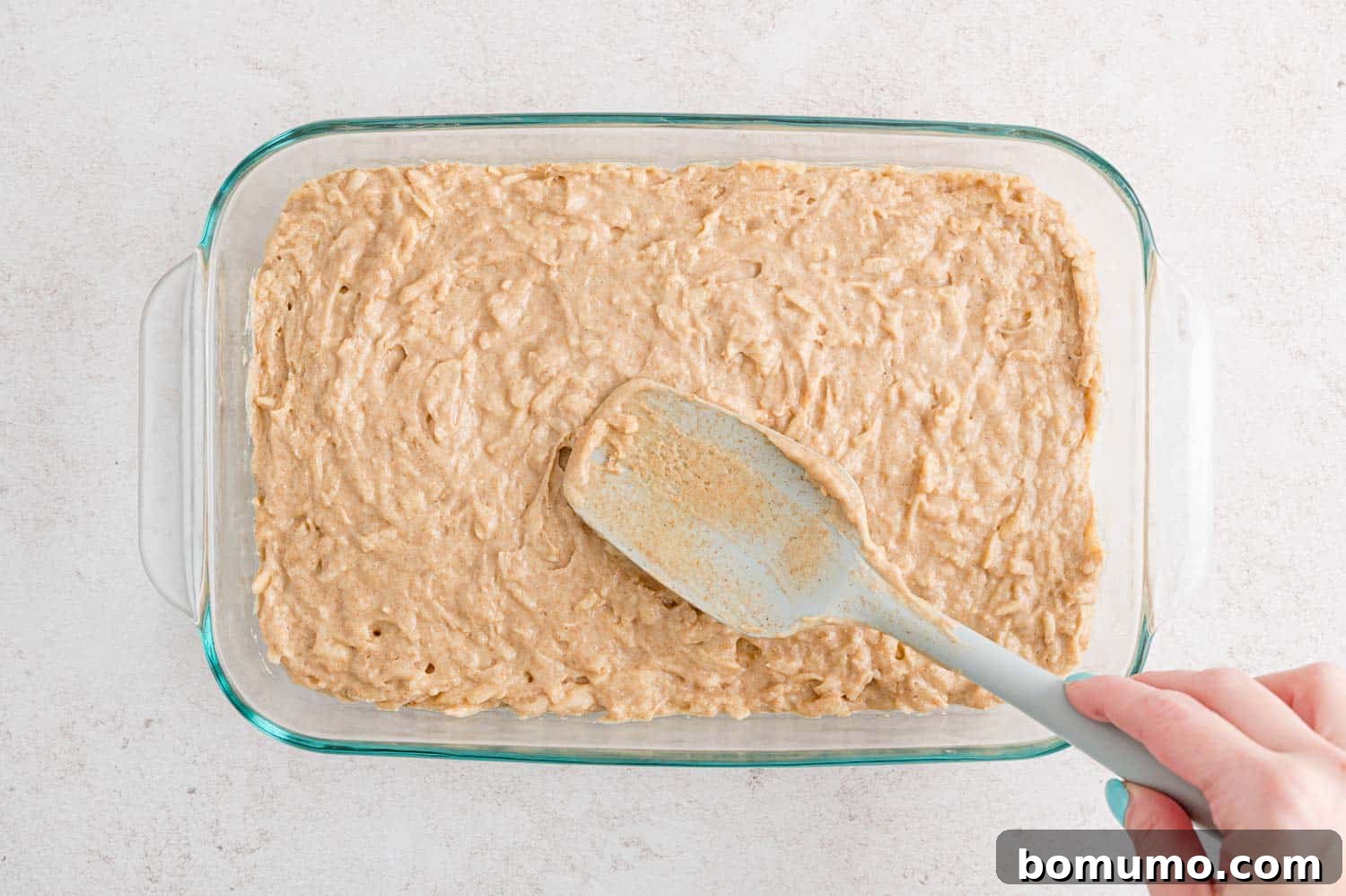Apple spice cake batter being spread into a glass baking dish.