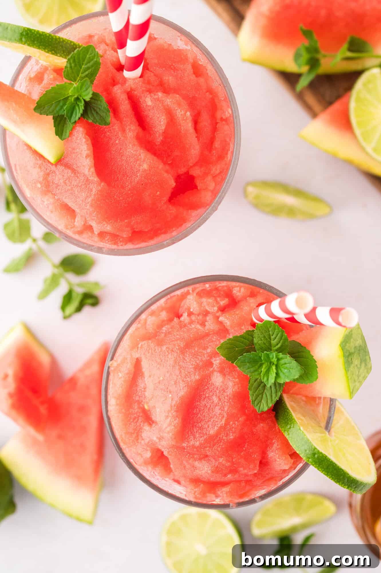 A top-down view of two perfectly prepared watermelon slushies, adorned with vibrant mint leaves and a wedge of lime, presented in stylish glasses.