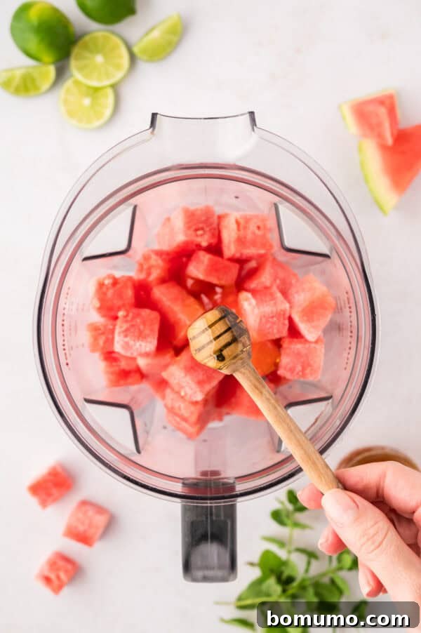 A stream of golden honey being drizzled into a blender filled with frozen watermelon, adding sweetness to the slushie mixture.