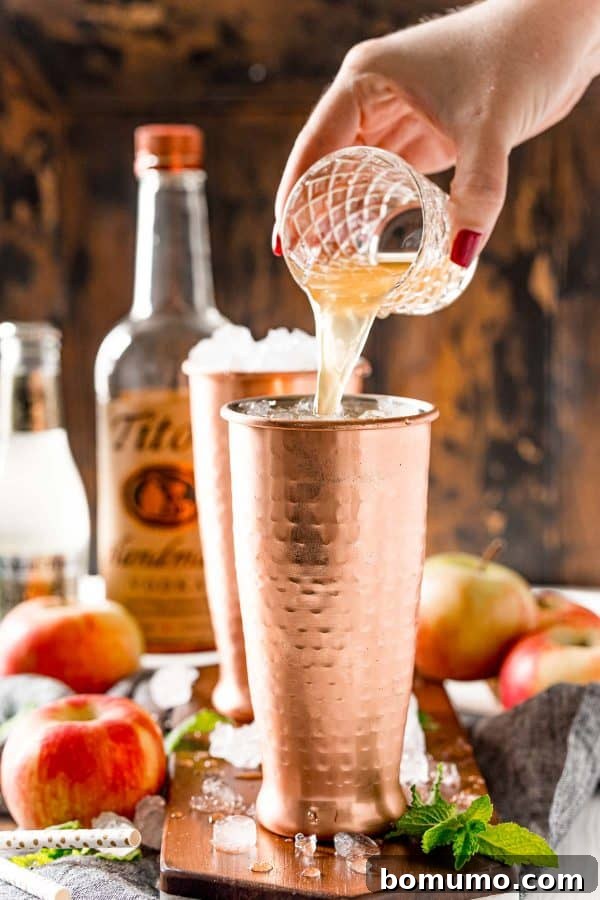 Apple Cider being poured into a glistening copper cup filled with ice, setting the stage for a delicious fall cocktail.