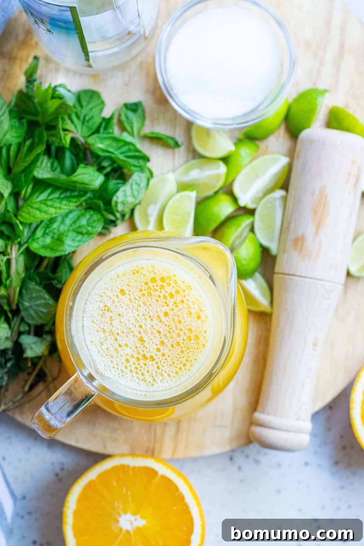Sun-Kissed Mojito 3 Essential ingredients for a homemade Orange Mojito: fresh orange juice, vibrant lime wedges, granulated sugar, and fragrant fresh mint leaves arranged on a rustic wooden surface.